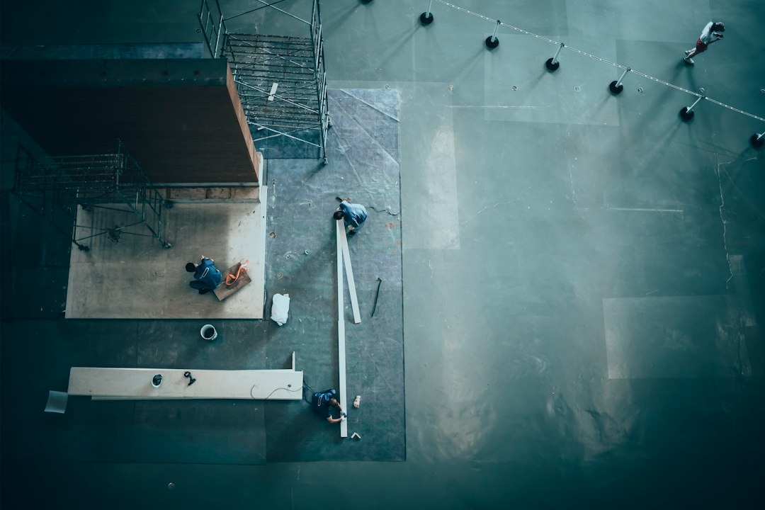 Three construction workers install materials inside a large warehouse.